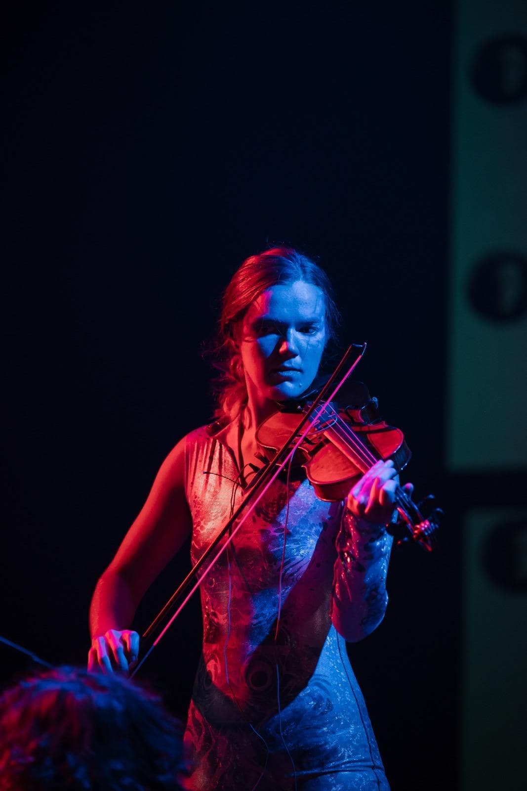 Annika Spegg in einer Performance mit Schmetterling-Kostüm und Mikrofon, vor einer Lichtinstallation.