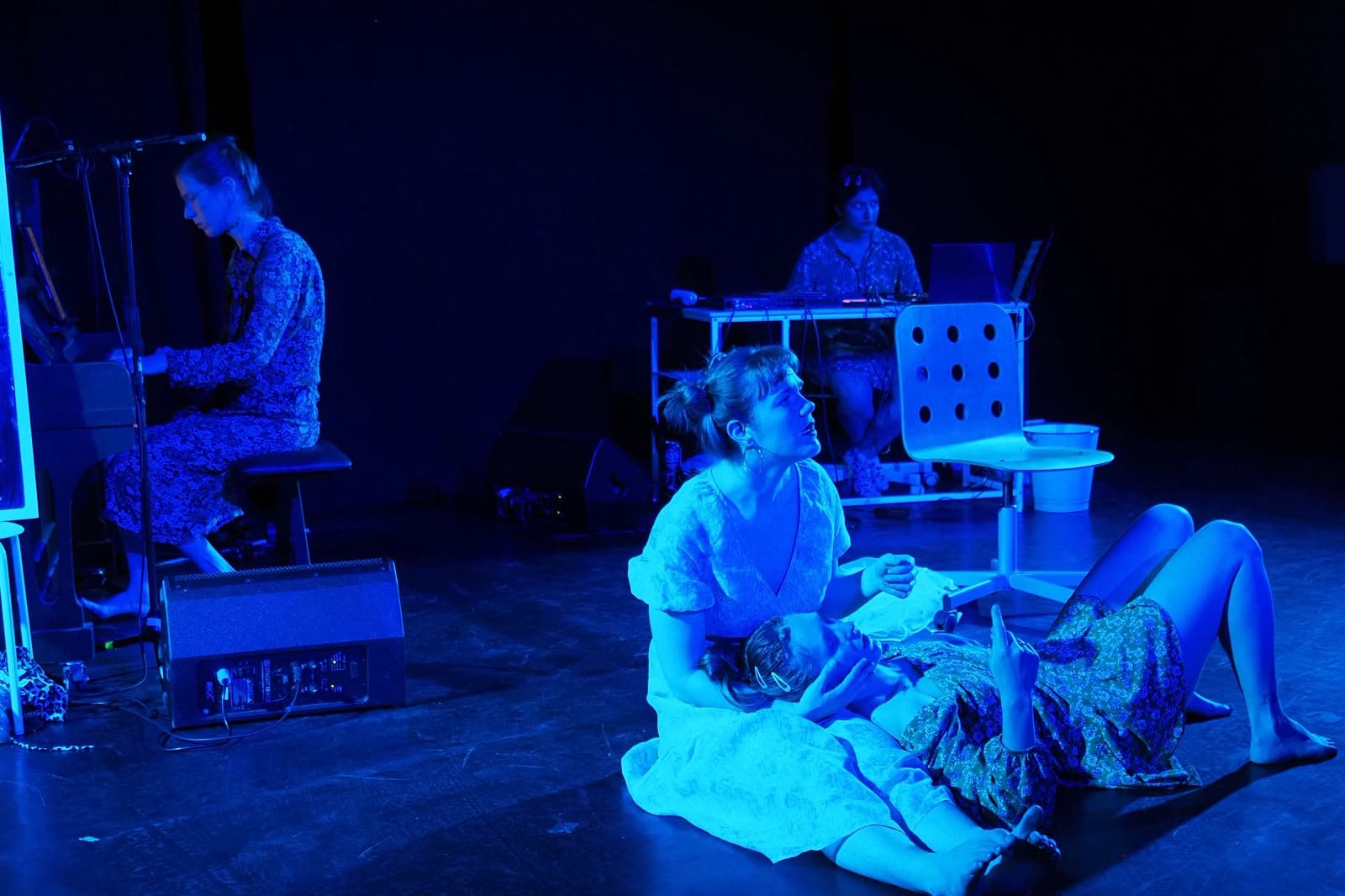 Szenenfoto Faust.Margarete — in blaues Licht getauchte Bühne mit Performerinnen am Boden, Harmonium und Live-Elektronik.