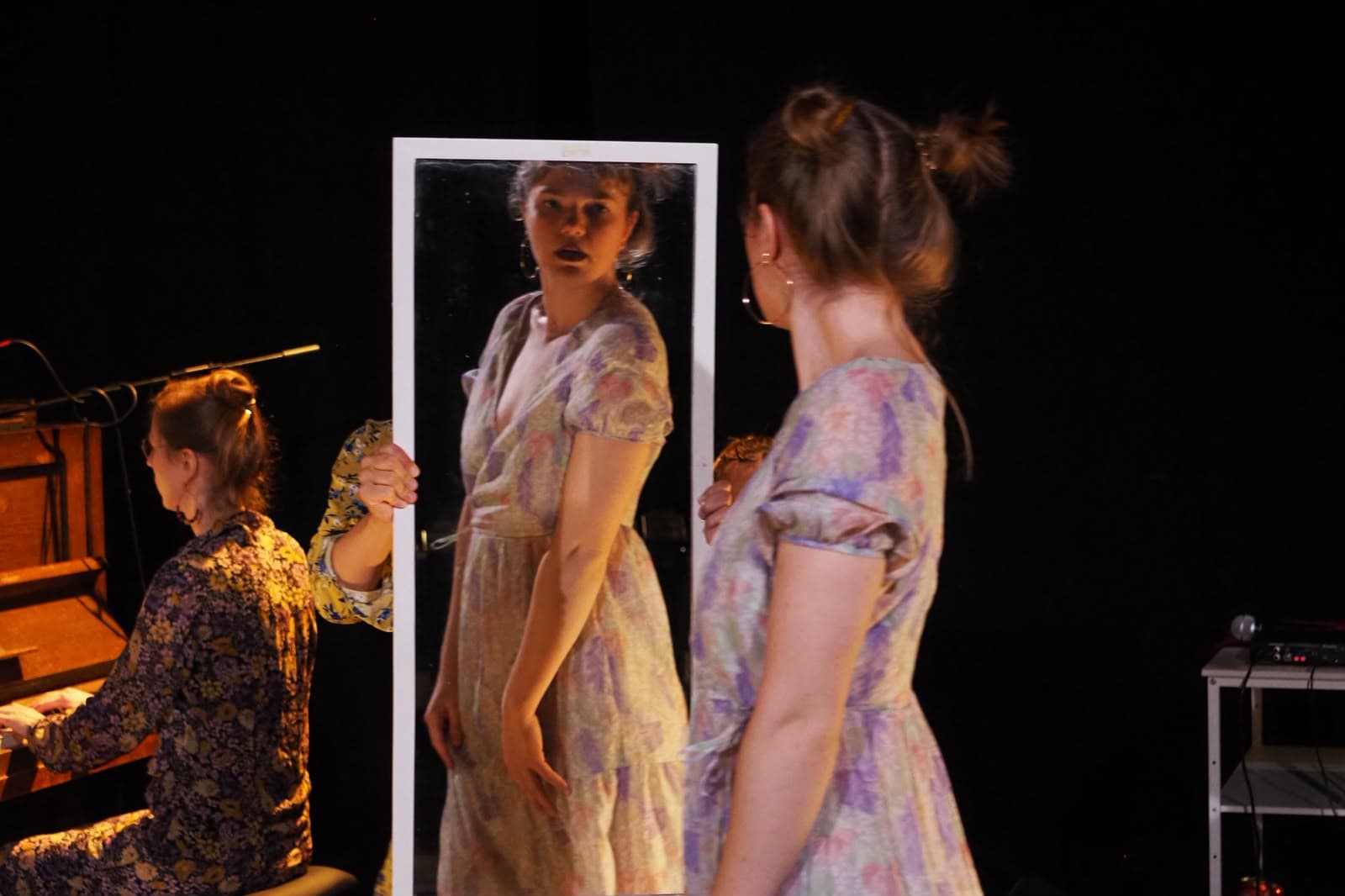 Faust.Margarete // GRETCHEN WANTS A FULL STORY — drei Performerinnen in Blümchenkleidern vor einem Standspiegel, links eine Spielerin am Harmonium.