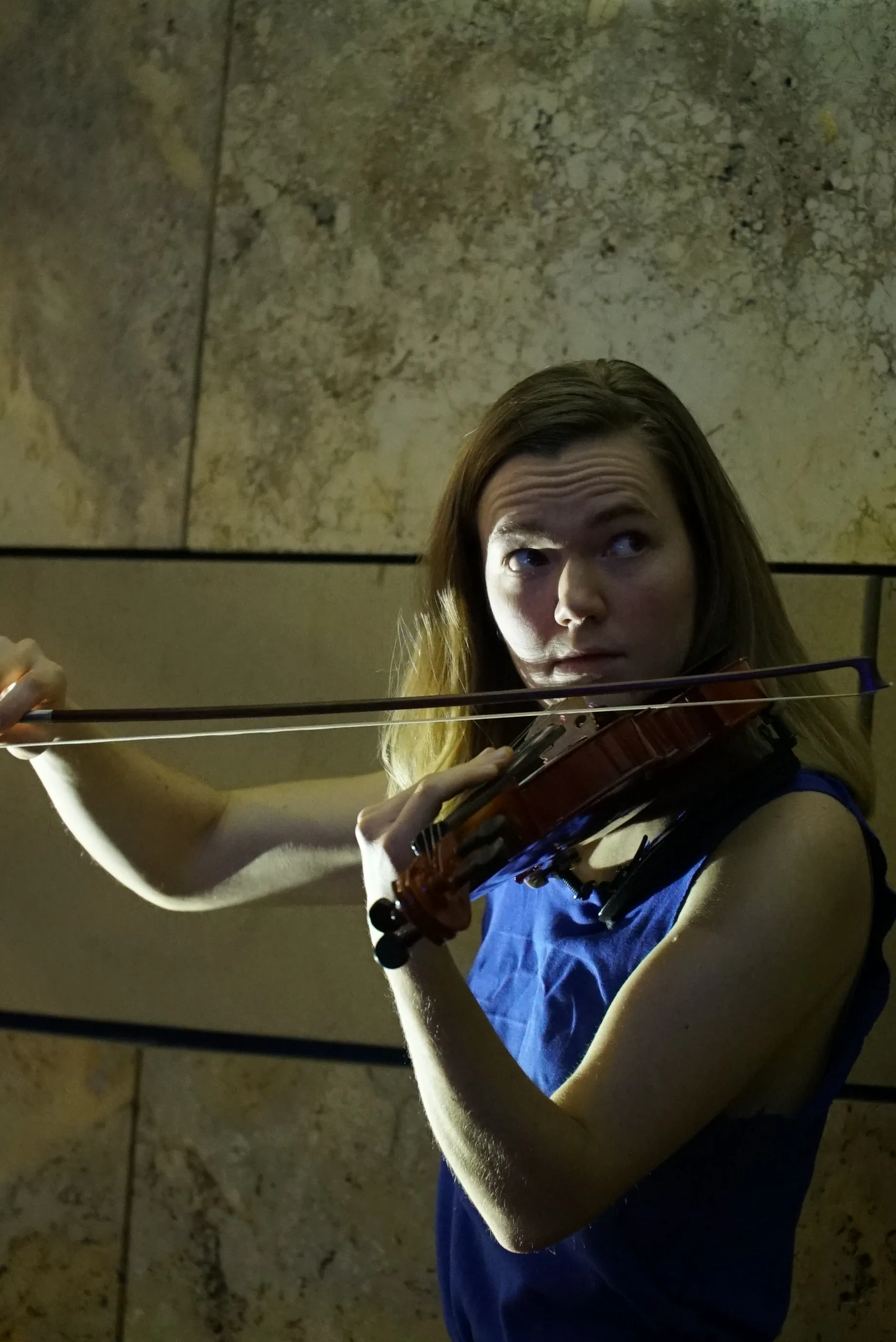 Annika Spegg im blauen Bühnenlicht spielt Geige aus der Vogelperspektive vor einem hellen, marmorierten Boden.
