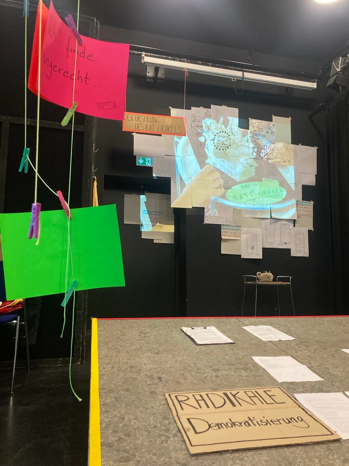 Lebendiges Archiv: hängende rote und grüne Karten („ich finde ungerecht…“) vor der Wand-Projektion „DAS RATS-ORAKEL“ und dem Pappschild „RADIKALE Demokratisierung“.