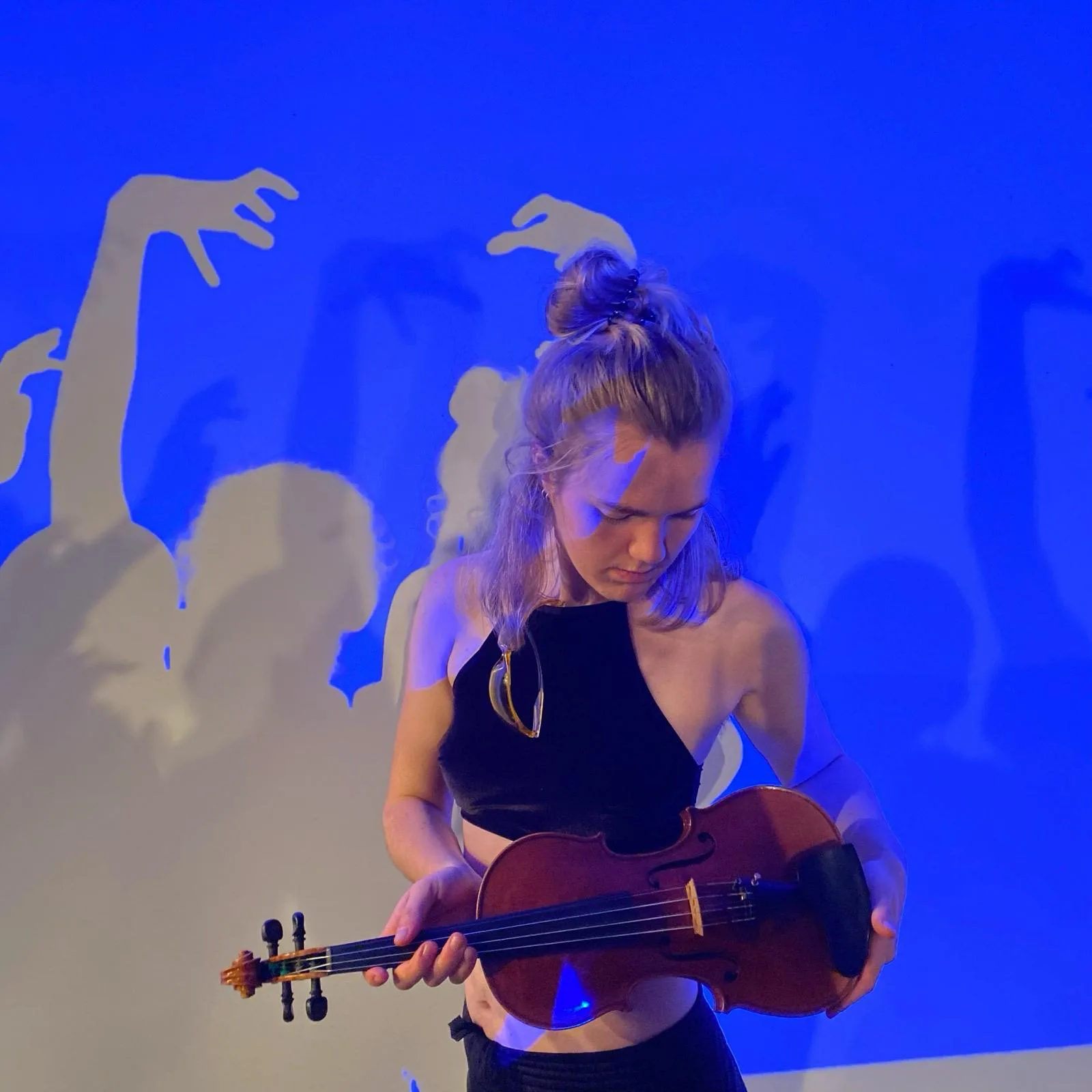 Annika Spegg hält Geige in blauem Bühnenlicht; an die Wand projiziert tanzen Hand-Schatten.