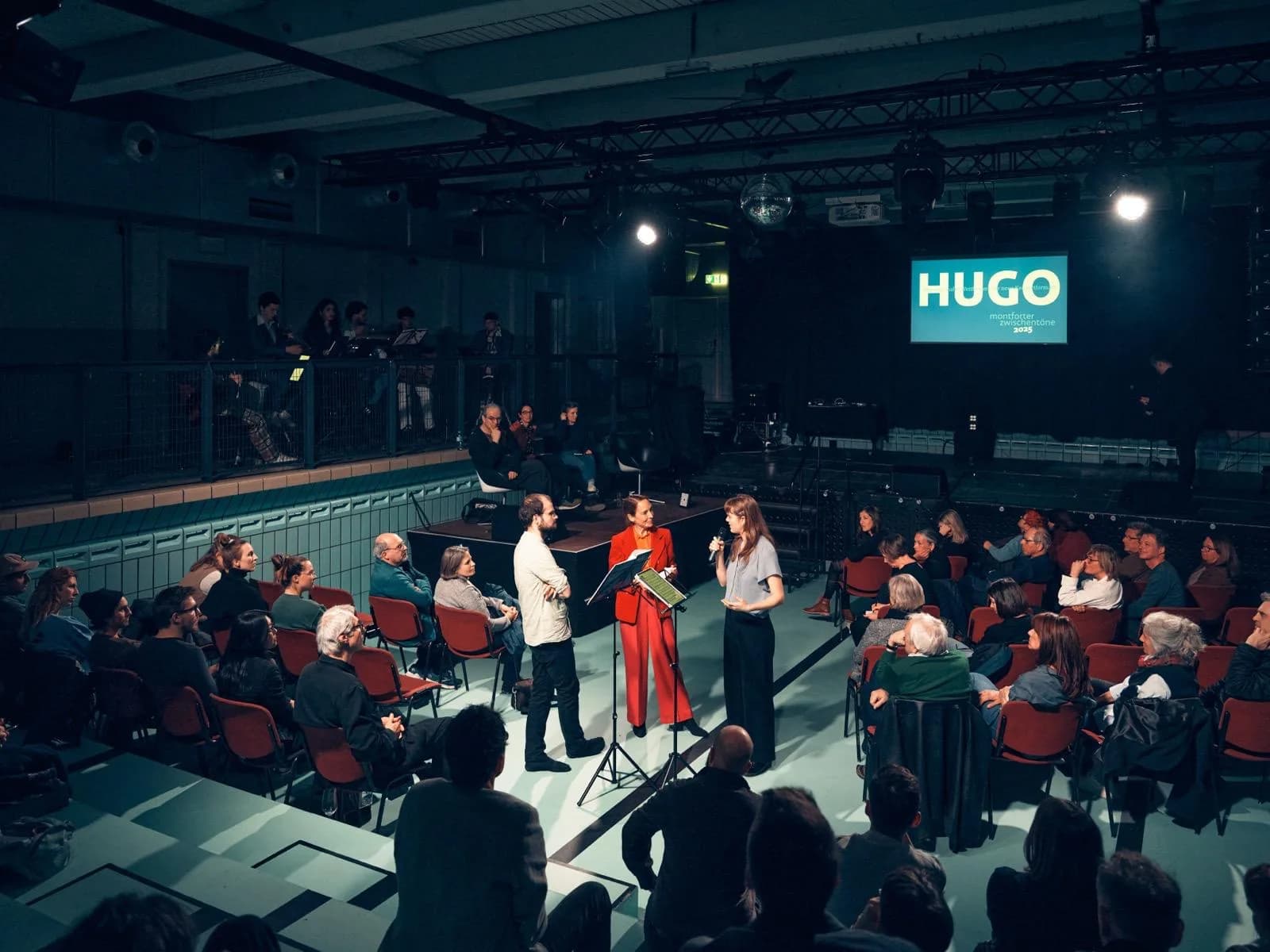 Bühnensituation des HUGO-Wettbewerbs der Montforter Zwischentöne; Annika Spegg spricht ins Mikrofon.