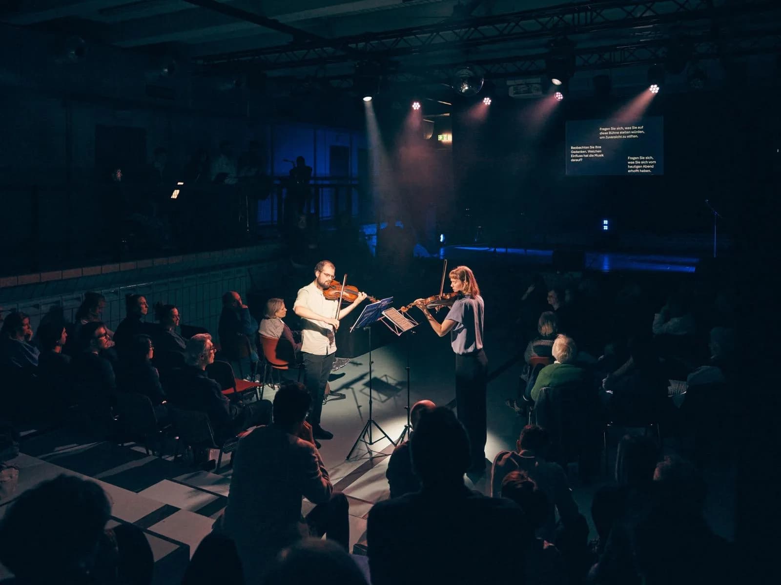 Annika Spegg spielt Geige im Konzert mit Robert Rülke (Duo Zwischen); Publikum sitzt um die Bühne.