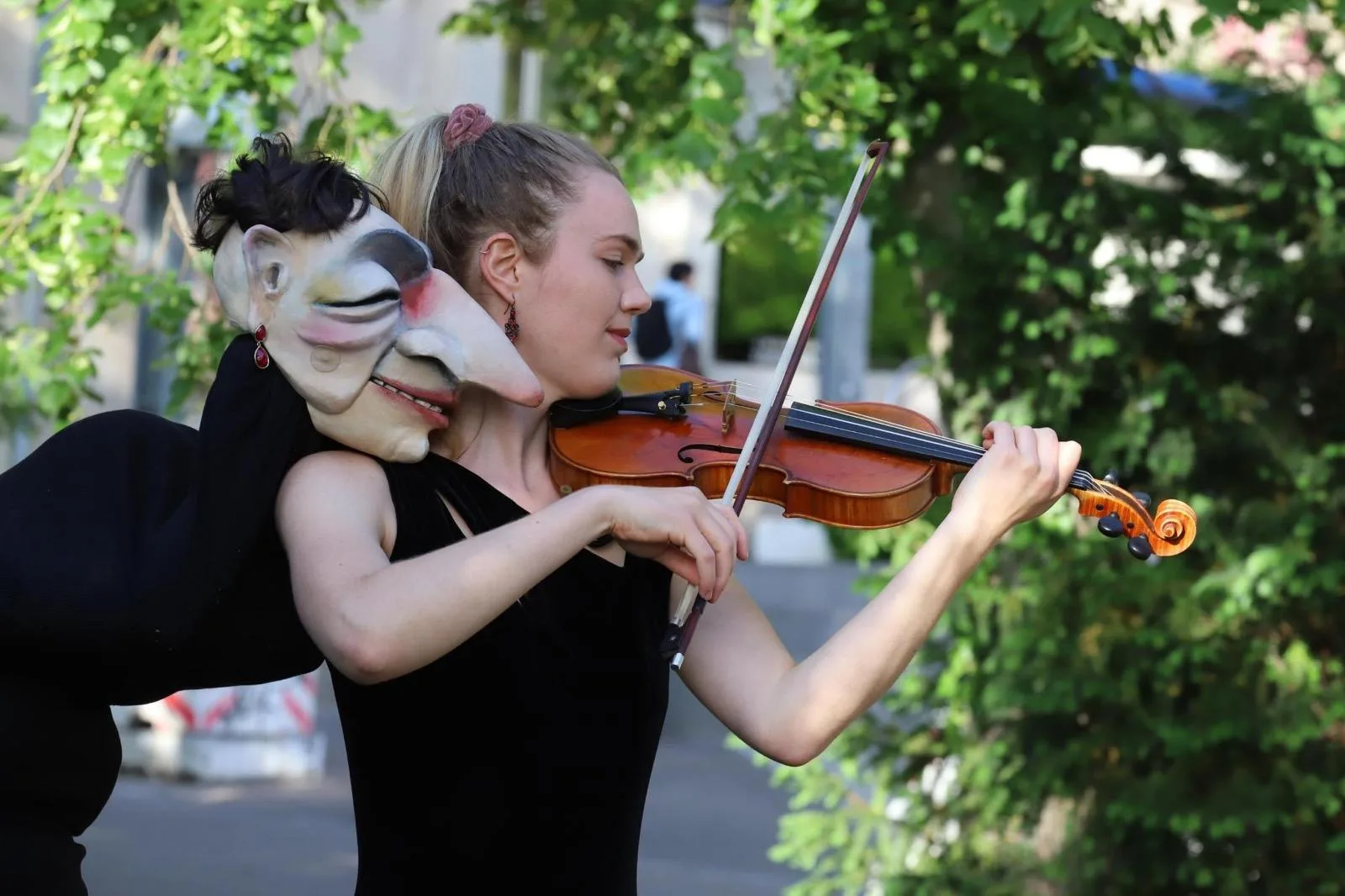 Annika Spegg spielt Geige im Profil; eine zweite Person hält neben ihr eine Maske ans Gesicht.
