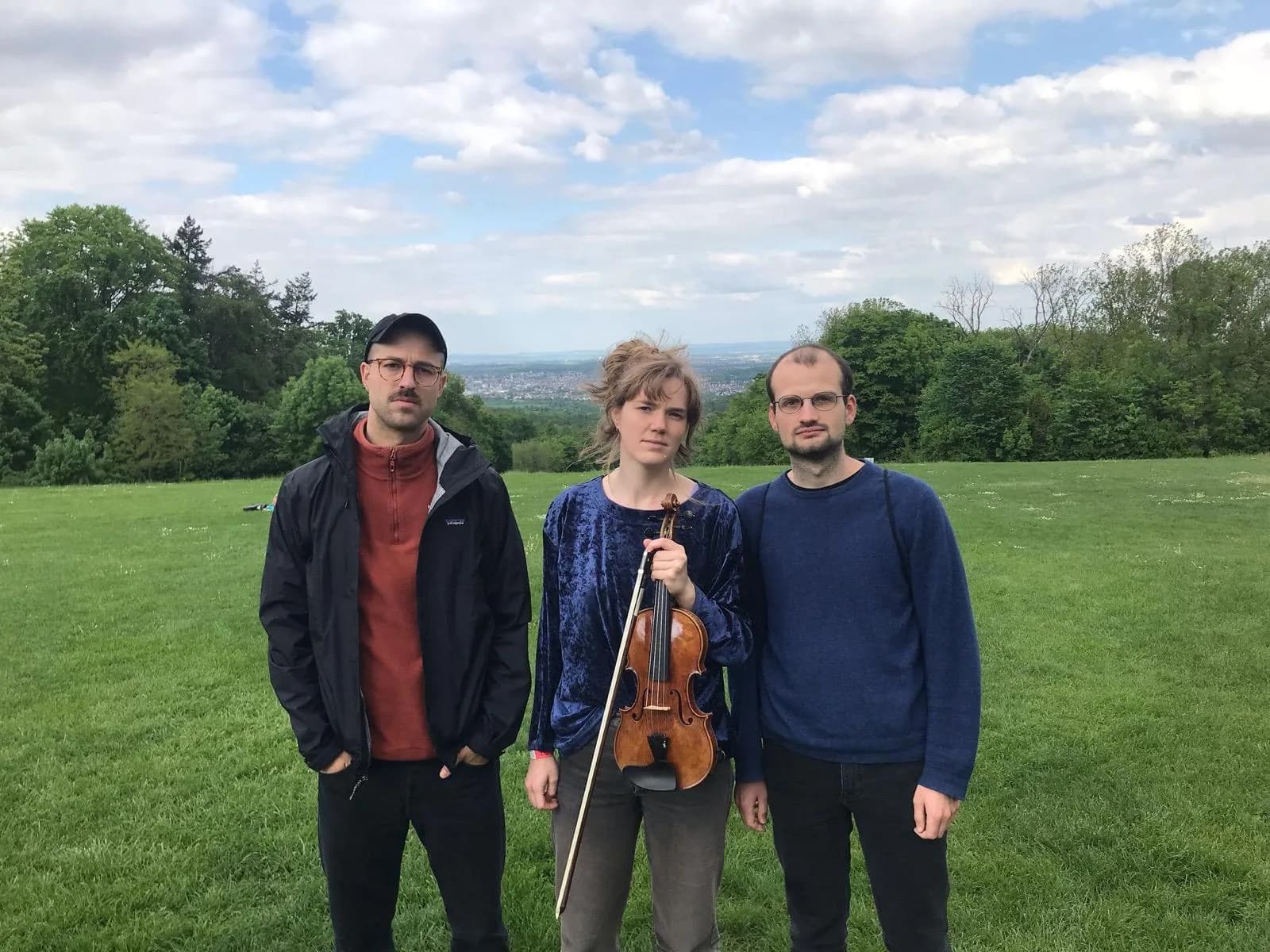 Annika Spegg mit Robert Rülke und einem weiteren Musiker auf einer Wiese vor einer Stadtkulisse.